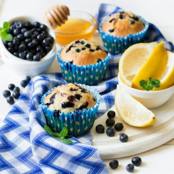 Homemade blueberry muffins with fresh berries, honey and lemon on white wooden background