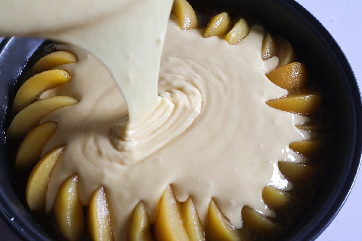 Cake batter being poured over the peaches.