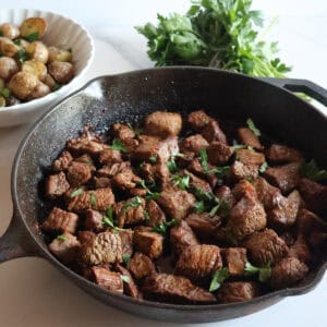 steak bites in a cast iron pan with potatoes and parsley.