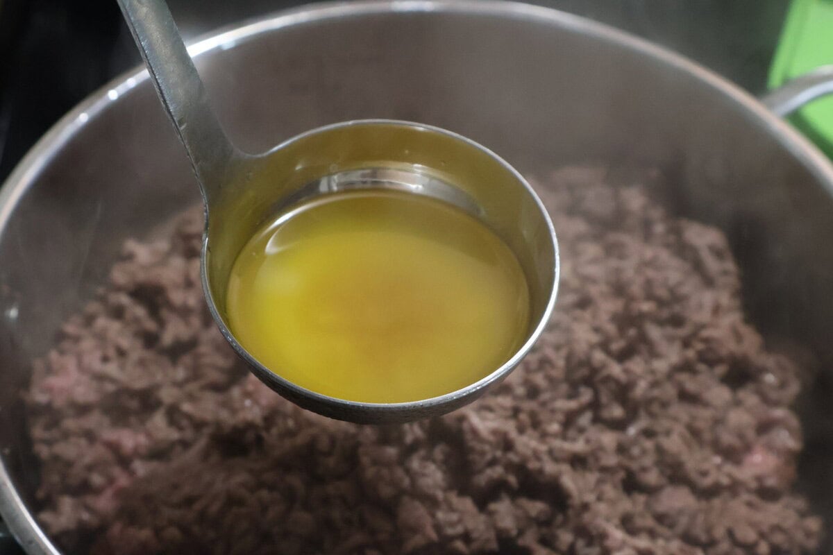 Ground beef in a pan with a ladle full of grease.