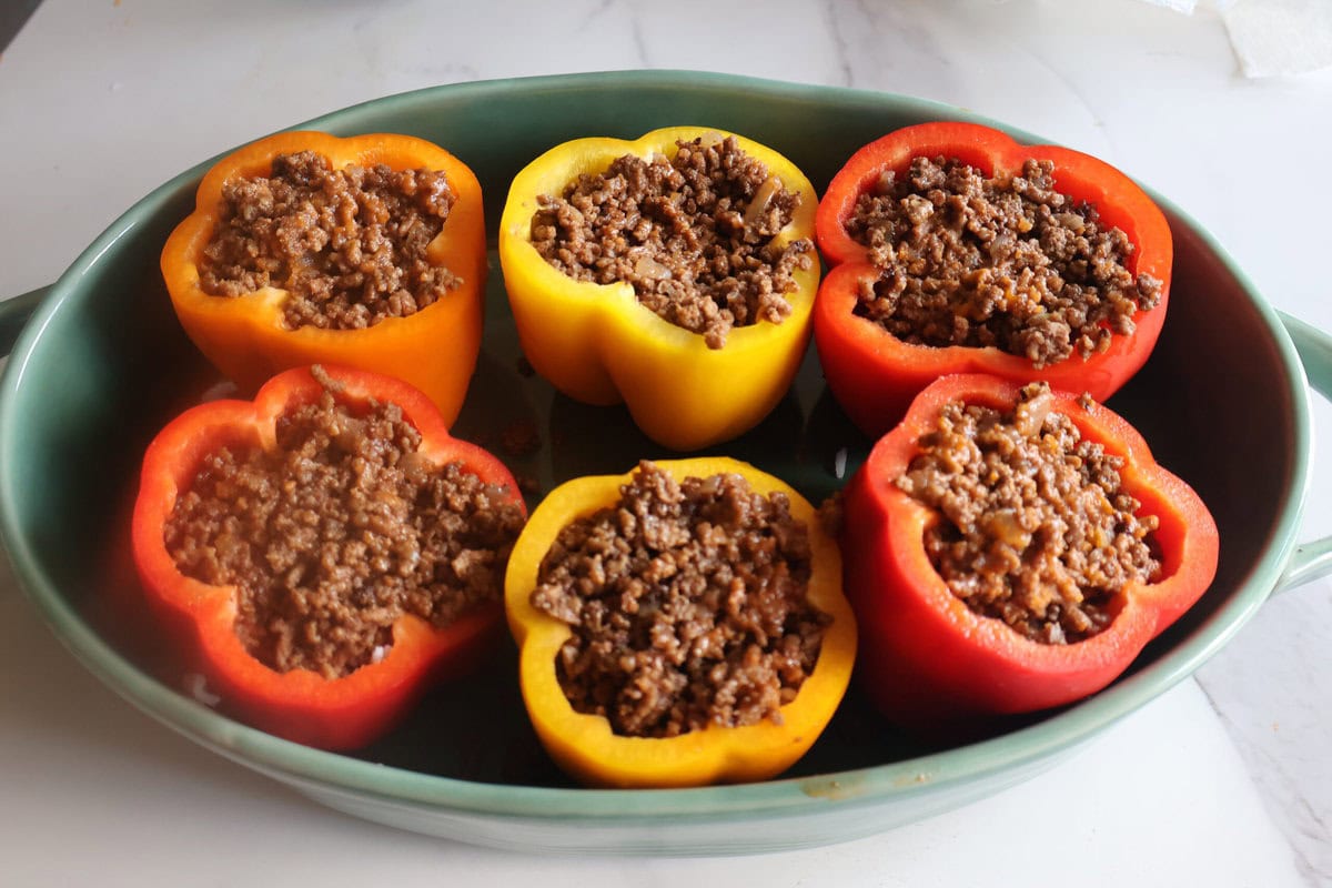 bell peppers in a green casserole dish stuffed with sloppy joe meat.