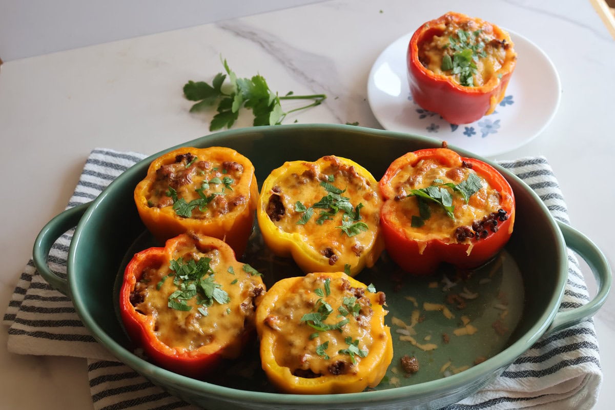 stuffed bell peppers in a green casserole dish with a gray and white striped tea towel.
