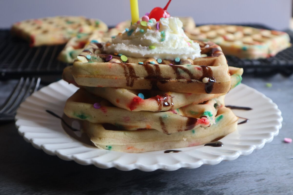 birthday waffles with confetti, whipped cream, and a cherry on a white plate.
