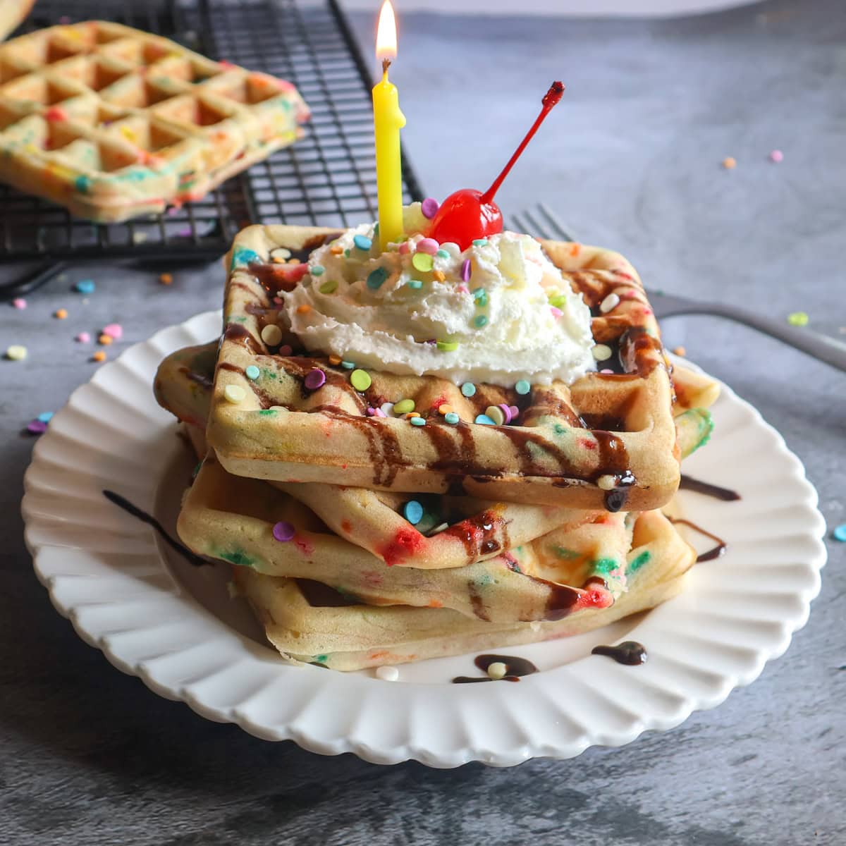 Stack of birthday waffles on a white plate with a yellow candle.