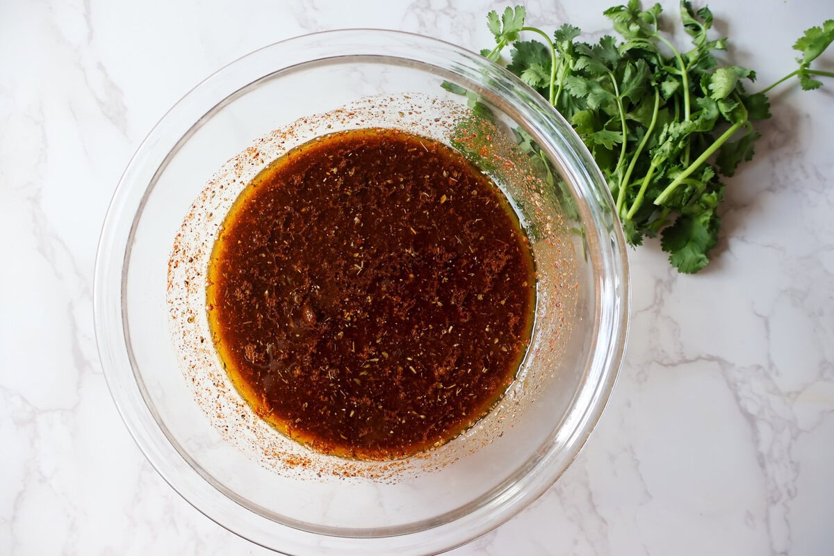 Grilled mexican chicken marinade in a glass bowl with cilantro on the side.