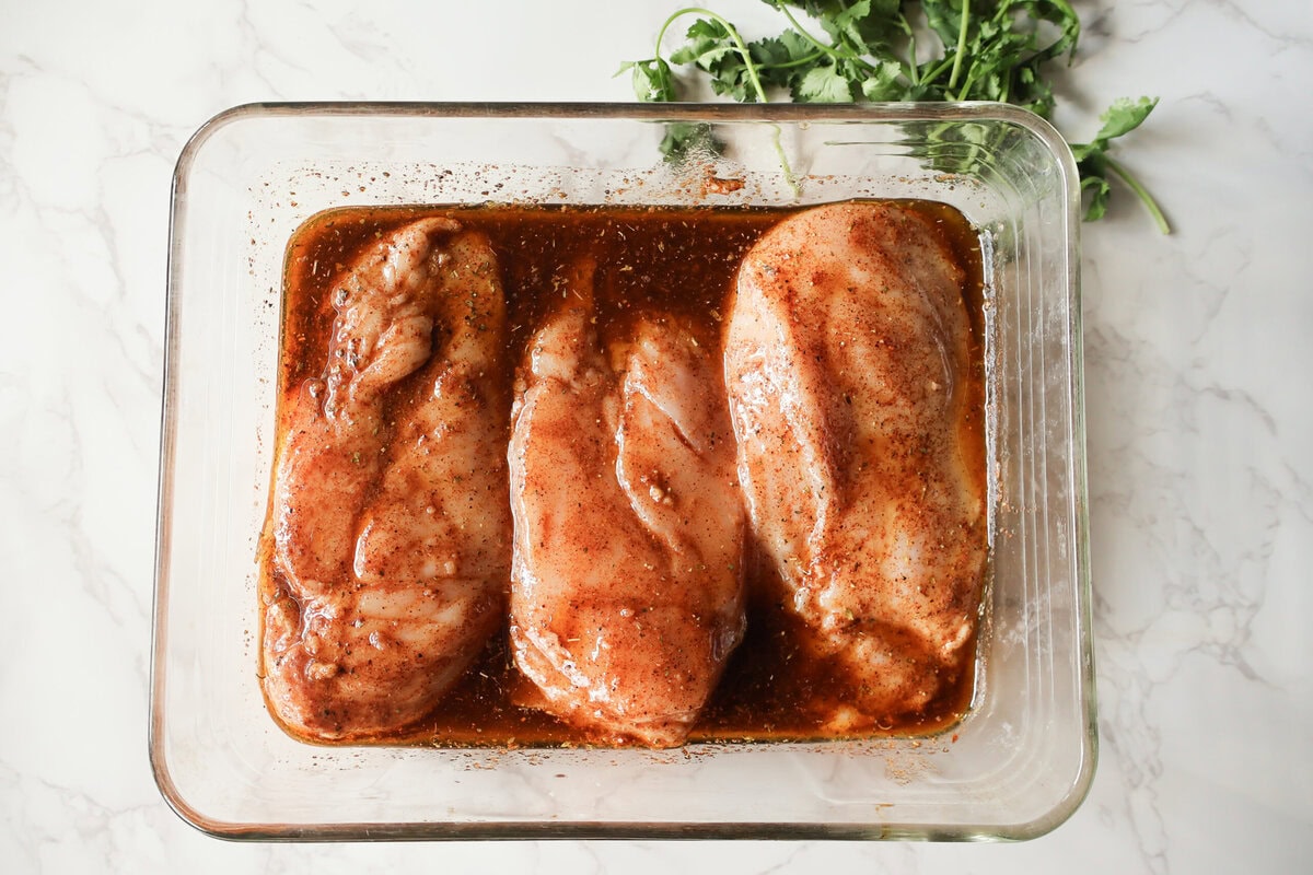 Chicken in the marinade sauce in a glass dish.