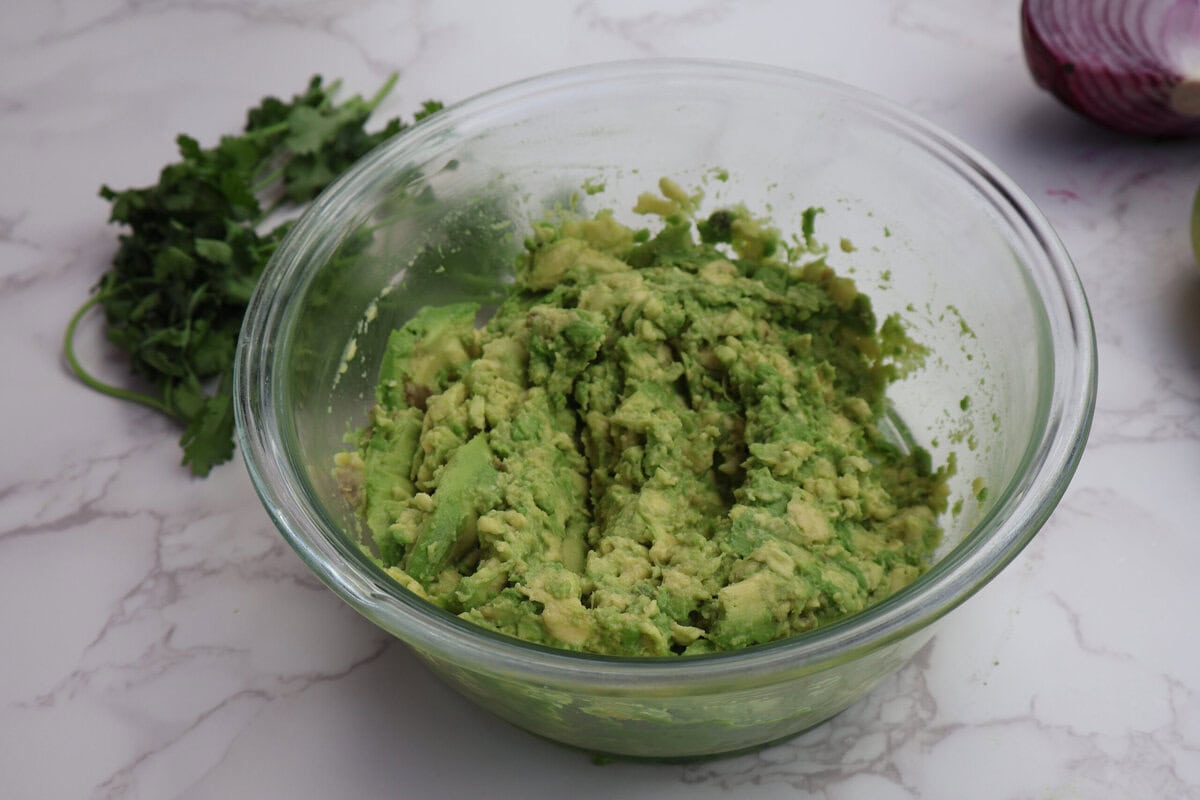 smashed avacado in a glass bowl with cilantro.
