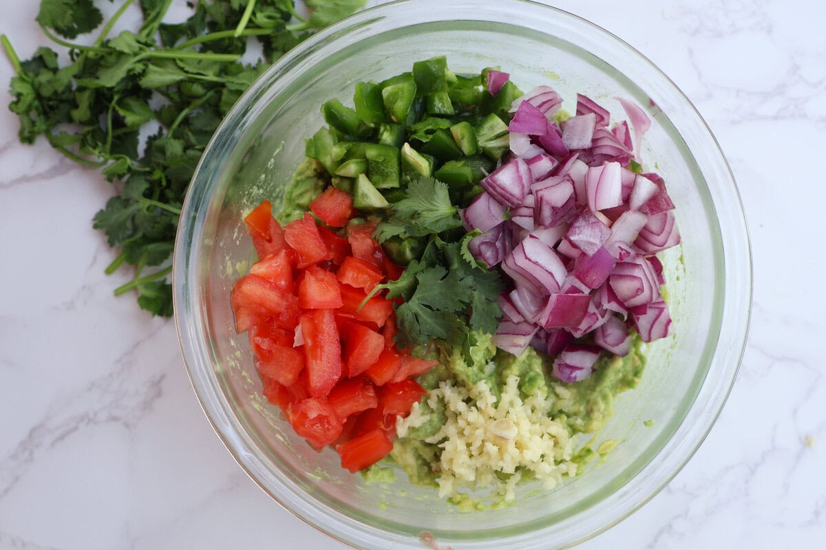 Guacamole ingredients in a clear bowl with cilantro.