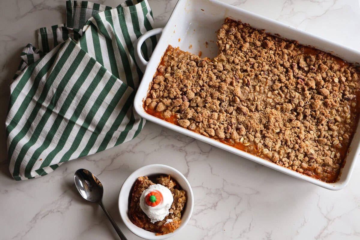 Pumpkin crumble in a white dish with a white and green striped towel and a single serving.