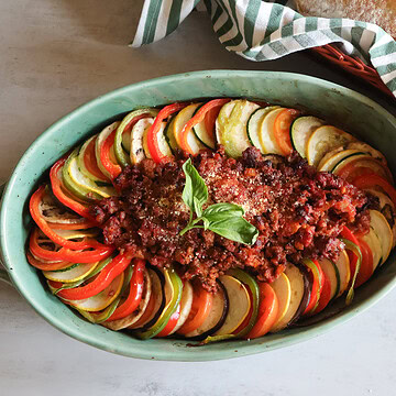 Ratatouille with meat in a green casserole dish with crusty bread.
