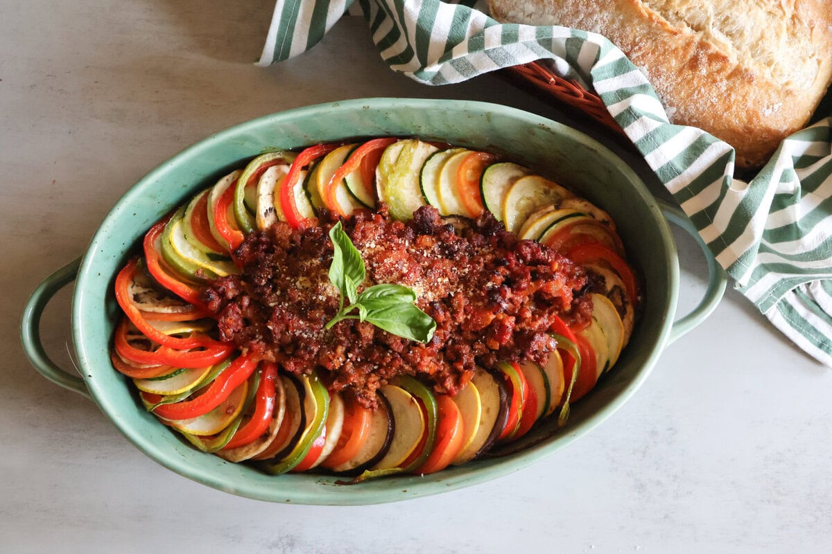Ratatouille in a green casserole dish and crusty bread with a green striped towel