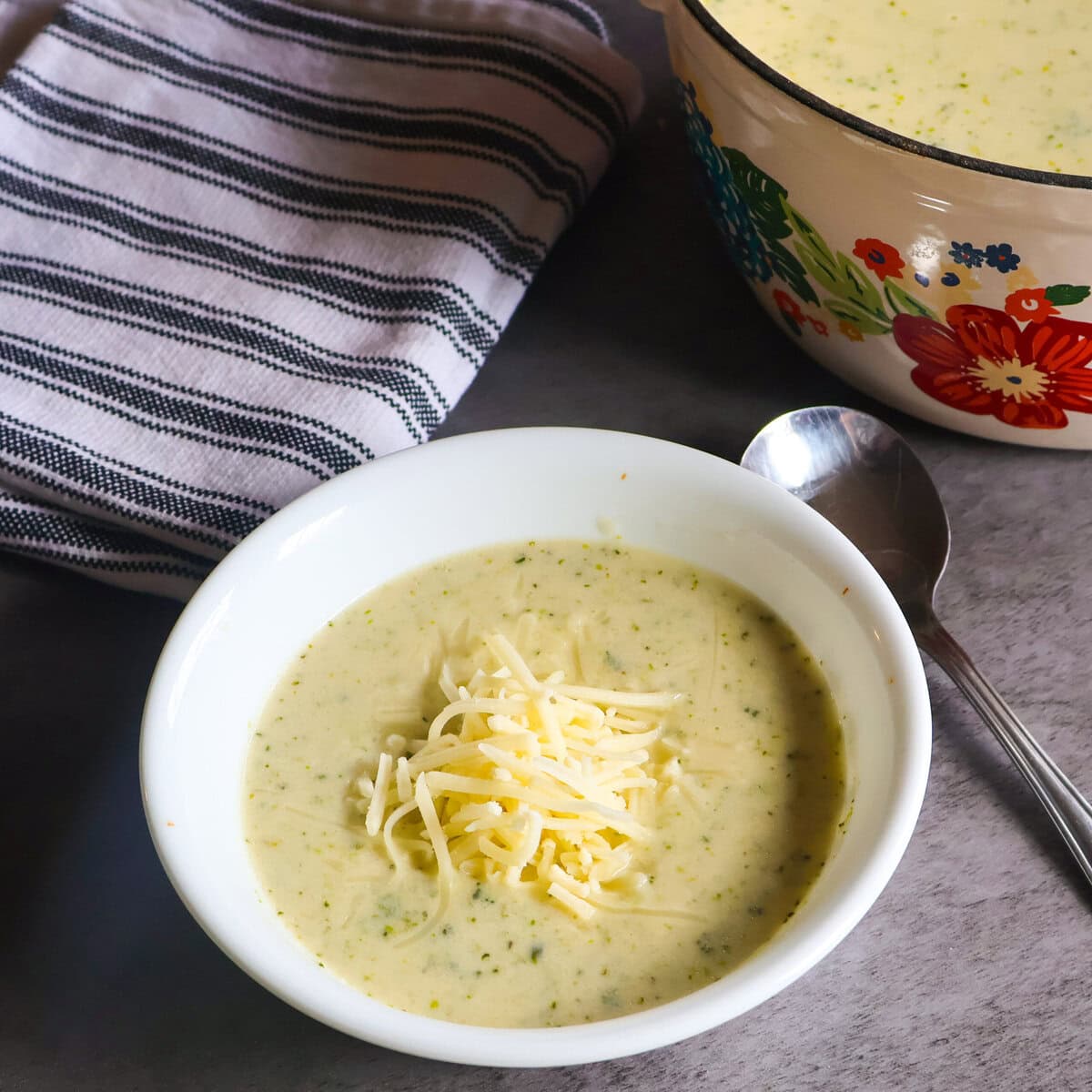 Broccolini and cheddar soup with a spoon abd a white and gray tea towel.