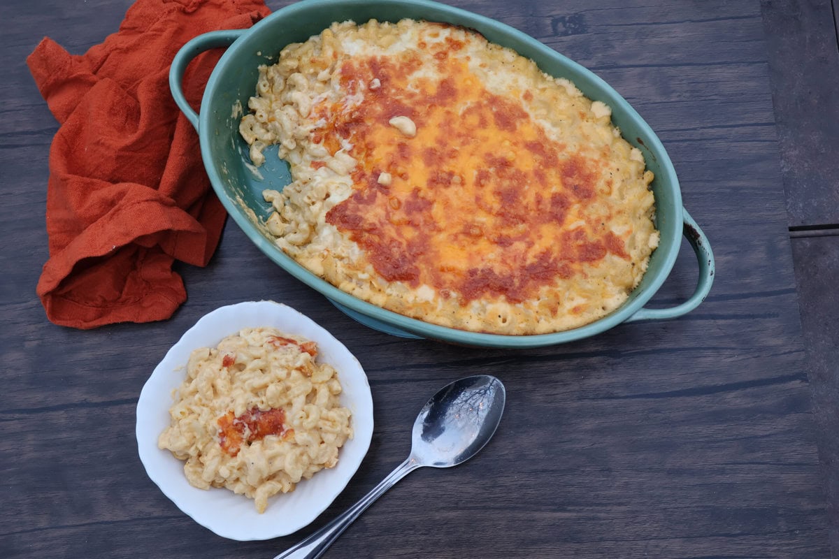 Baked macaroni and cheese in a green casserole dish and in a white bowl with a spoon and an orange napkin.