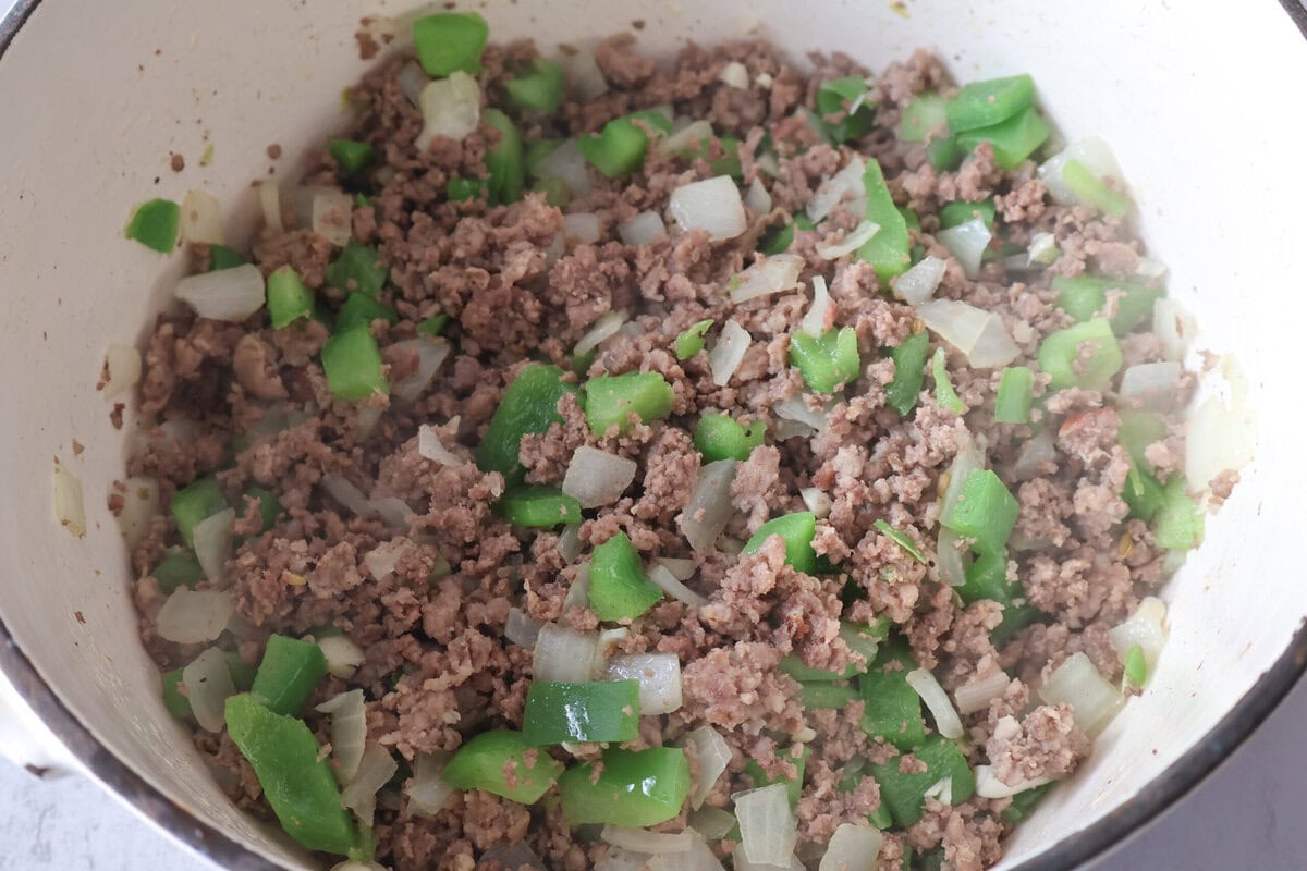 beef and sausagr with garlic, onion, and green pepper in a pot.