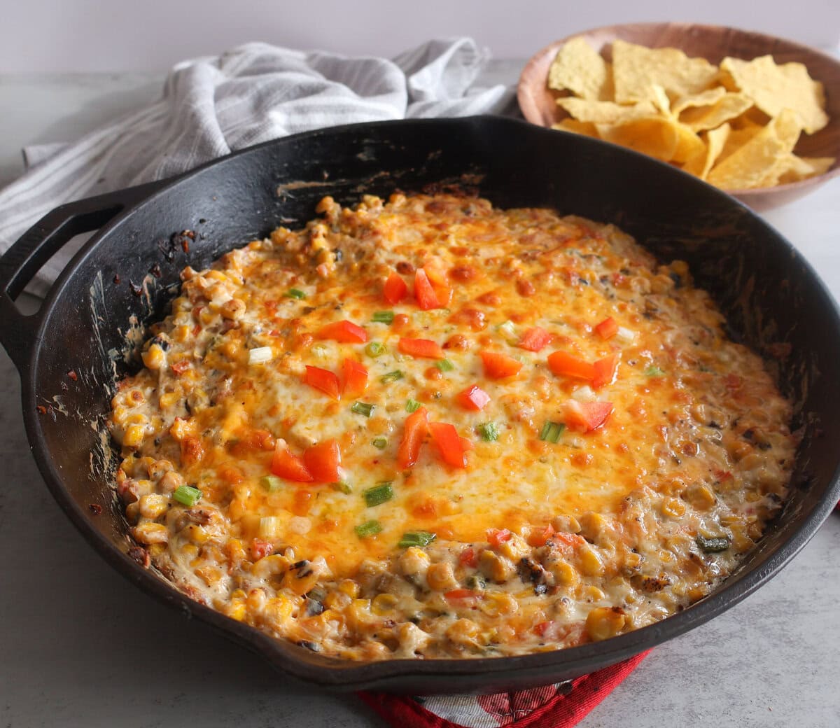 Cheesy corn dip in a cast iron skillet with tortilla chips and a napkin.