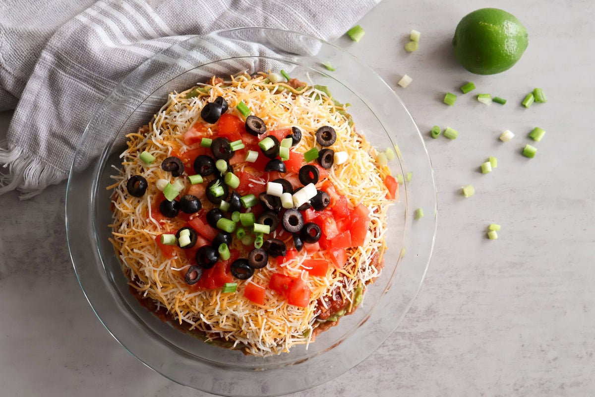5 layer dip in a glass bowl with a gray towel and lime.
