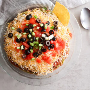 5 layer taco dip in a glass dish with a spoon.