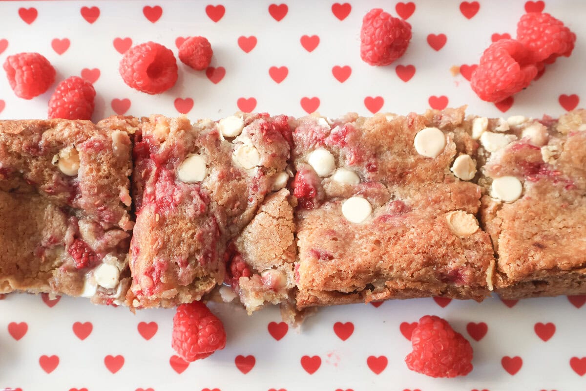 White chocolare raspberry blondie squares on a heart plate with fresh raspberries.