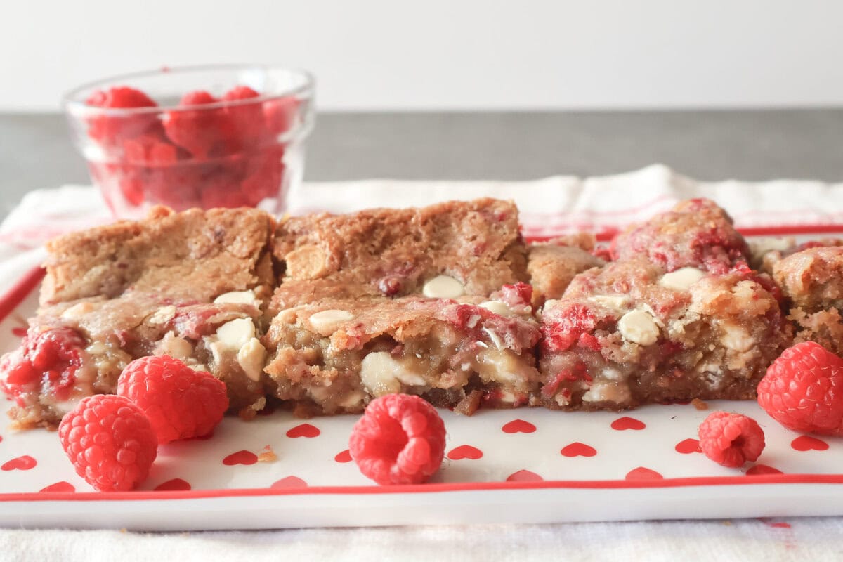 White chocolate raspberry blondies on a heart plate with fresh raspberries.