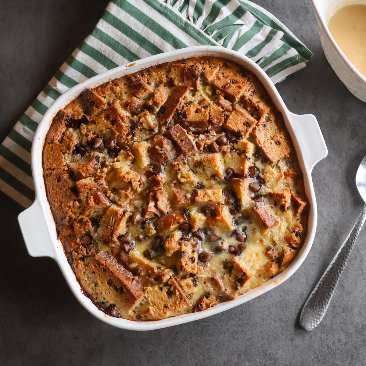Irish Soda bread Pudding in a white casserole dish with a green striped tea towel and a spoon.