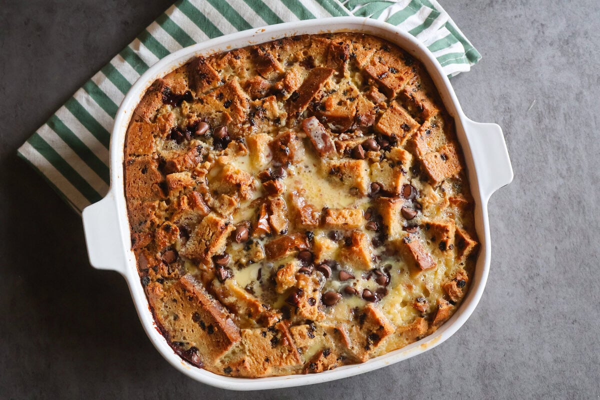 Irish Soda Bread Pudding Recipe in a white casserole dish with a green striped tea towel.