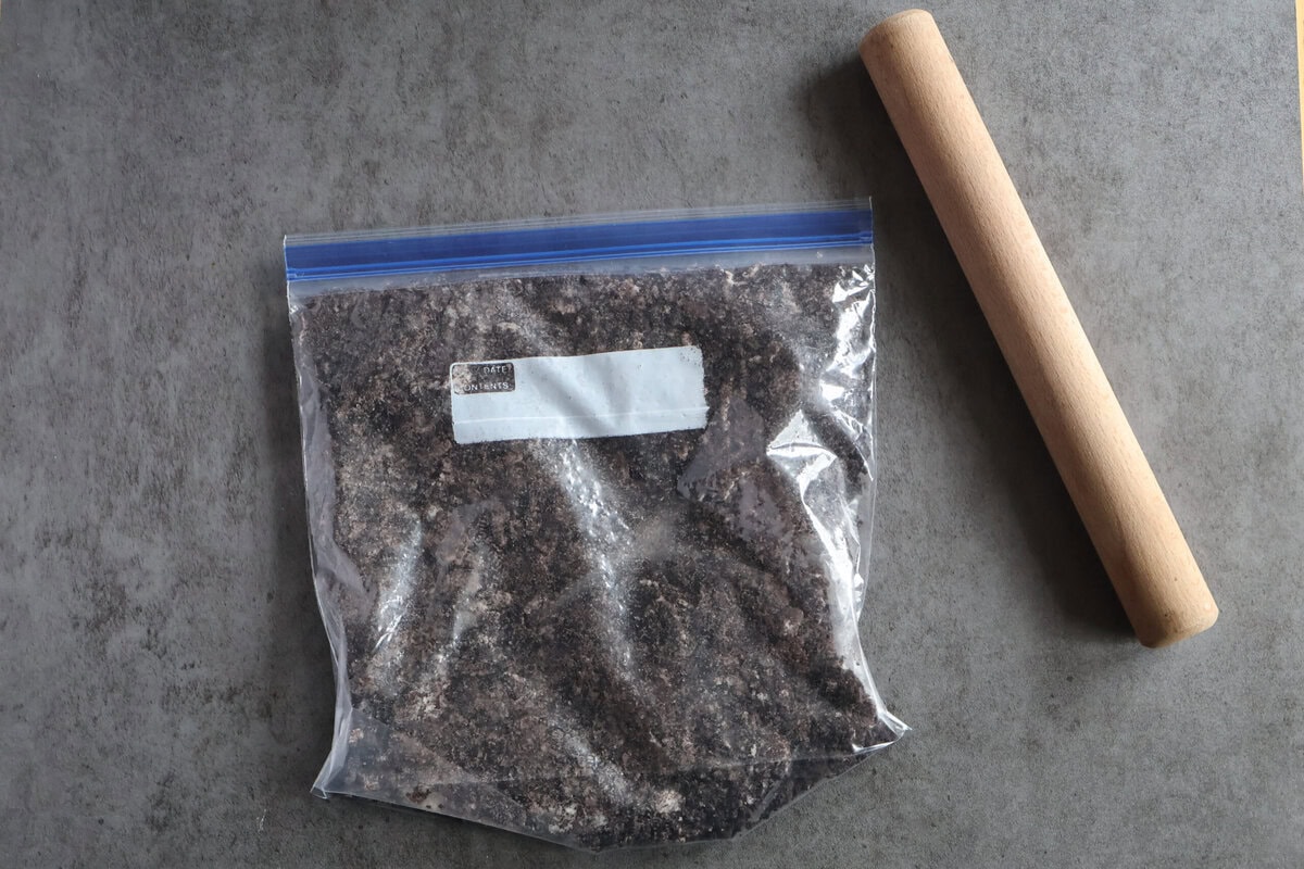 A zip lock baggie of crushed oreo cookies and a rolling pin.