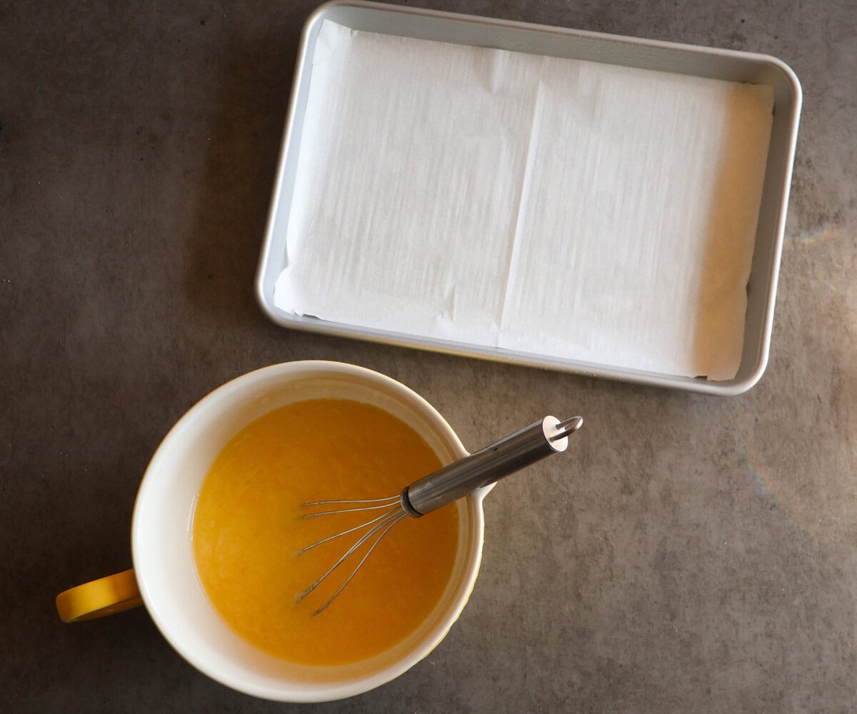 Parchment paper lined pan with a bowl of melted butter and sugar.
