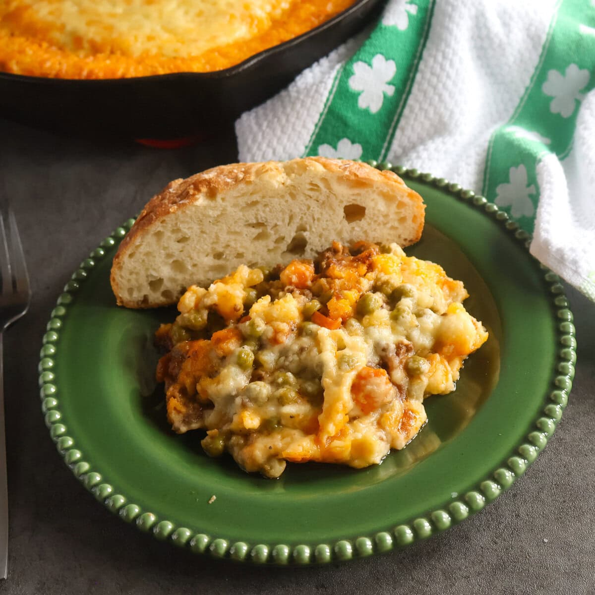 Guinness Cottage Pie on a green plate with a piece of bread with a green and white tea towel.