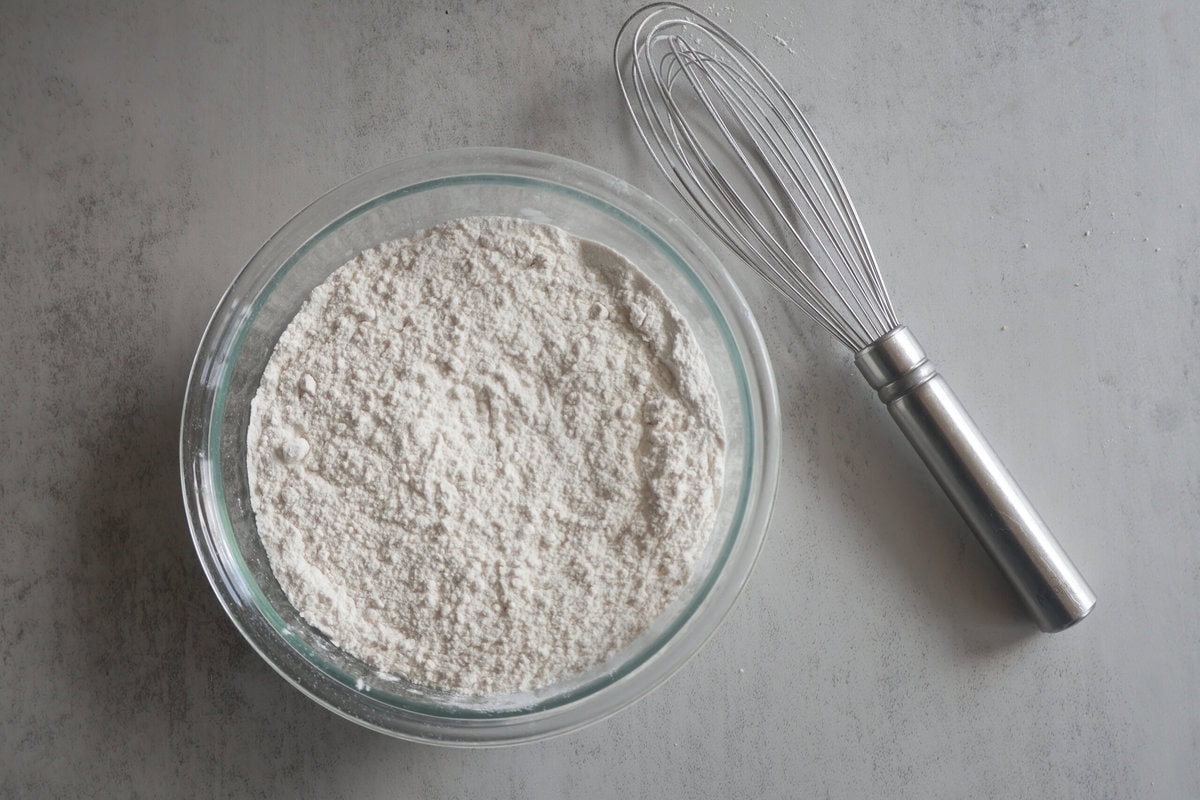 Dry ingredients in a glass bowl with a whisk.
