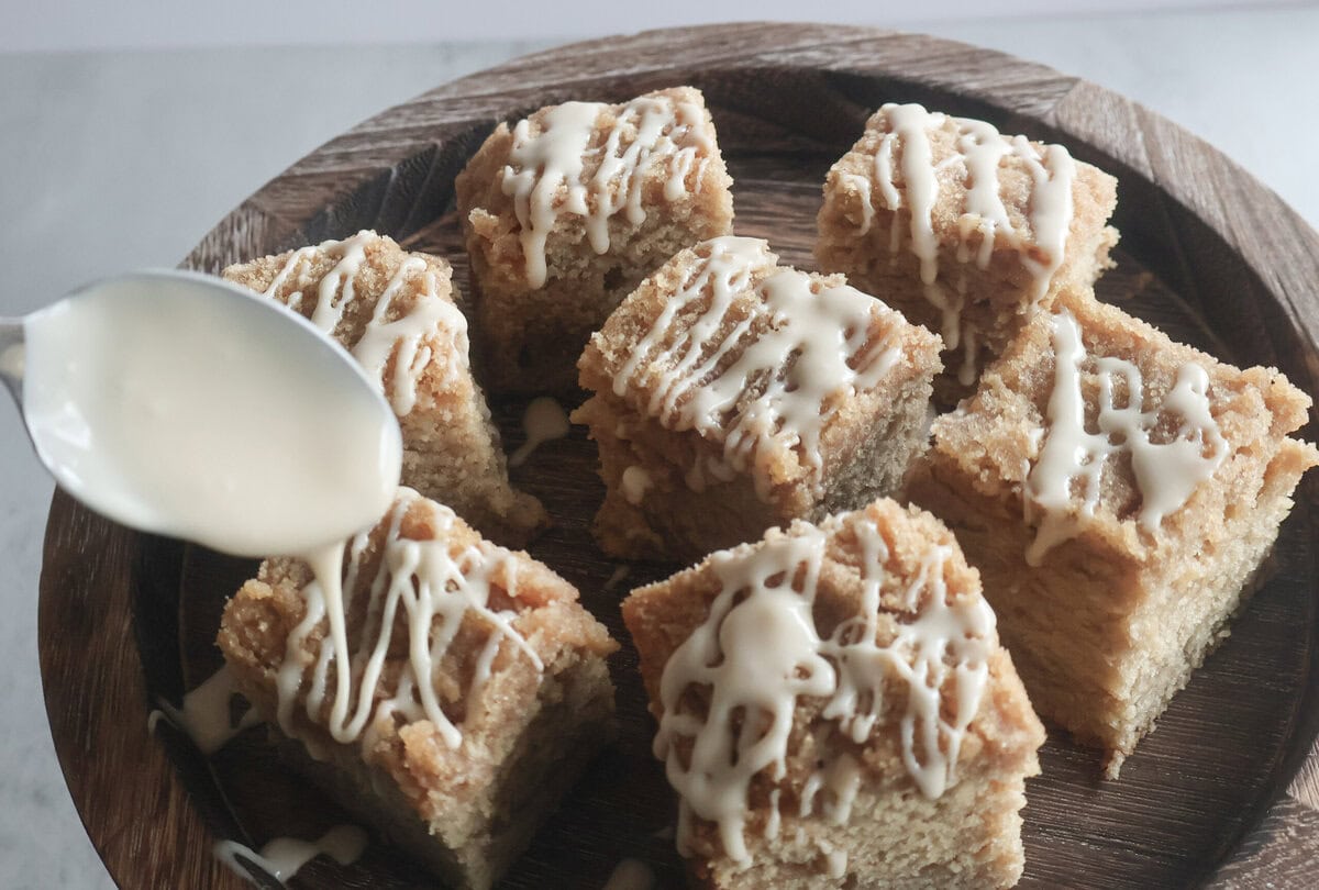Irish coffee cake squares on a wood cake stand with a spoon and glaze.
