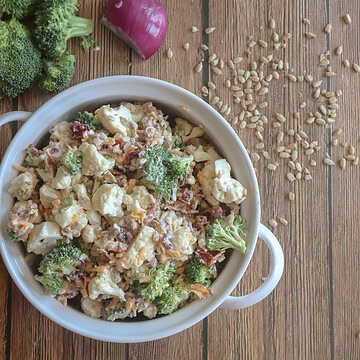 Creamy Cauliflower and Broccoli salad in a white dish with sunflower seeds.