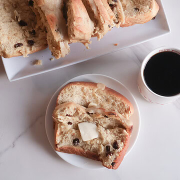 slice of spiced hot cross buns loaf on a white plate with a cup of coffee.