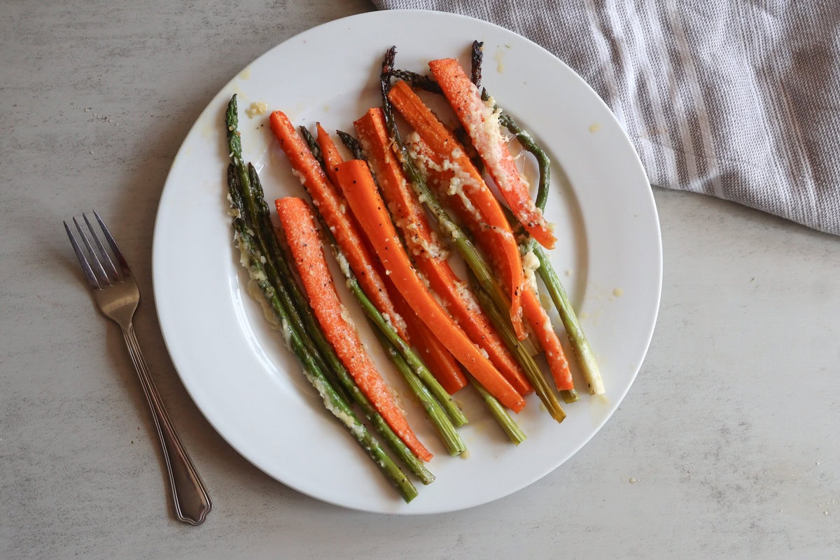 Honey garlic roasted asparagus and carrots on a white plate with a fork.