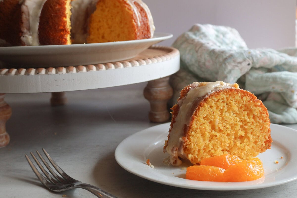 Mandarin Orange Bundt cake on a cake stand with a slice on a cake plate with a fork.