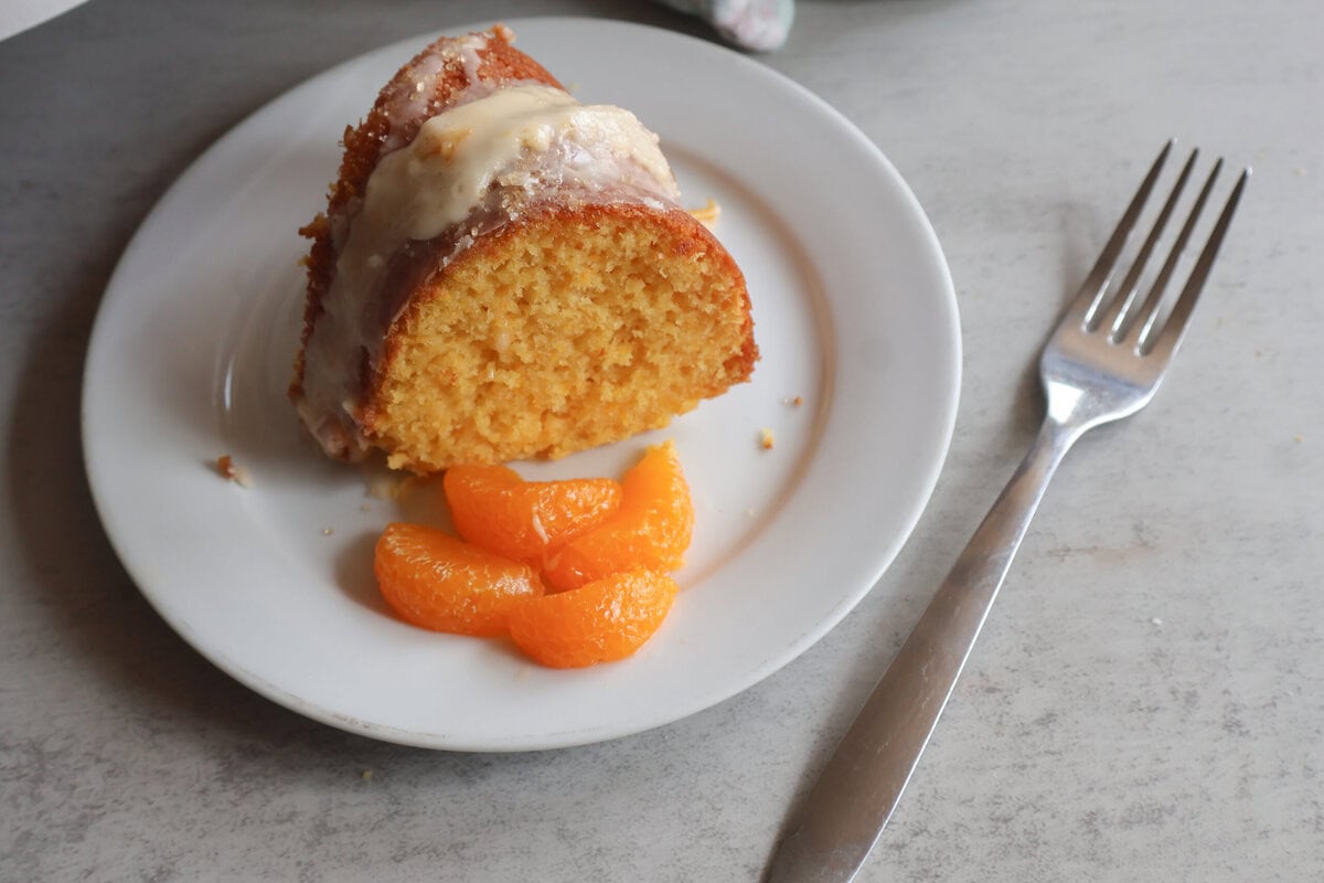 A single piece of mandarin orange bundt cake on a white plate with a fork.