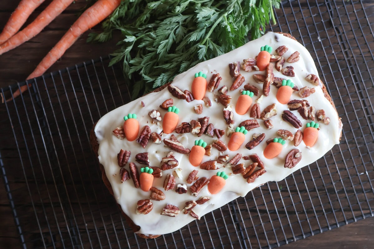 finished carrot cake pound cake with fresh carrots on a wire rack.