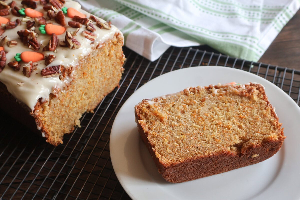 carrot cake pound cake on a wire rack with a slice on a white plate.