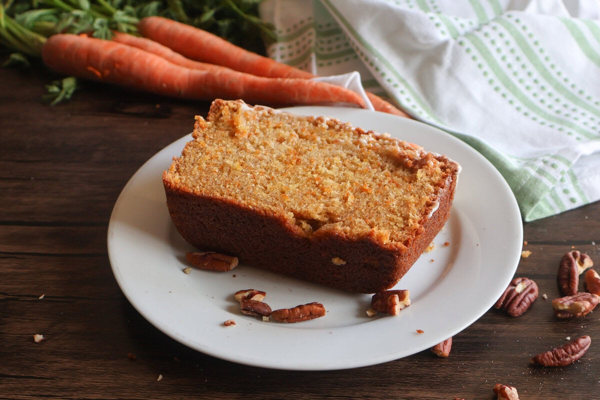 carrot cake pound cake with fresh carrots on a white plate.