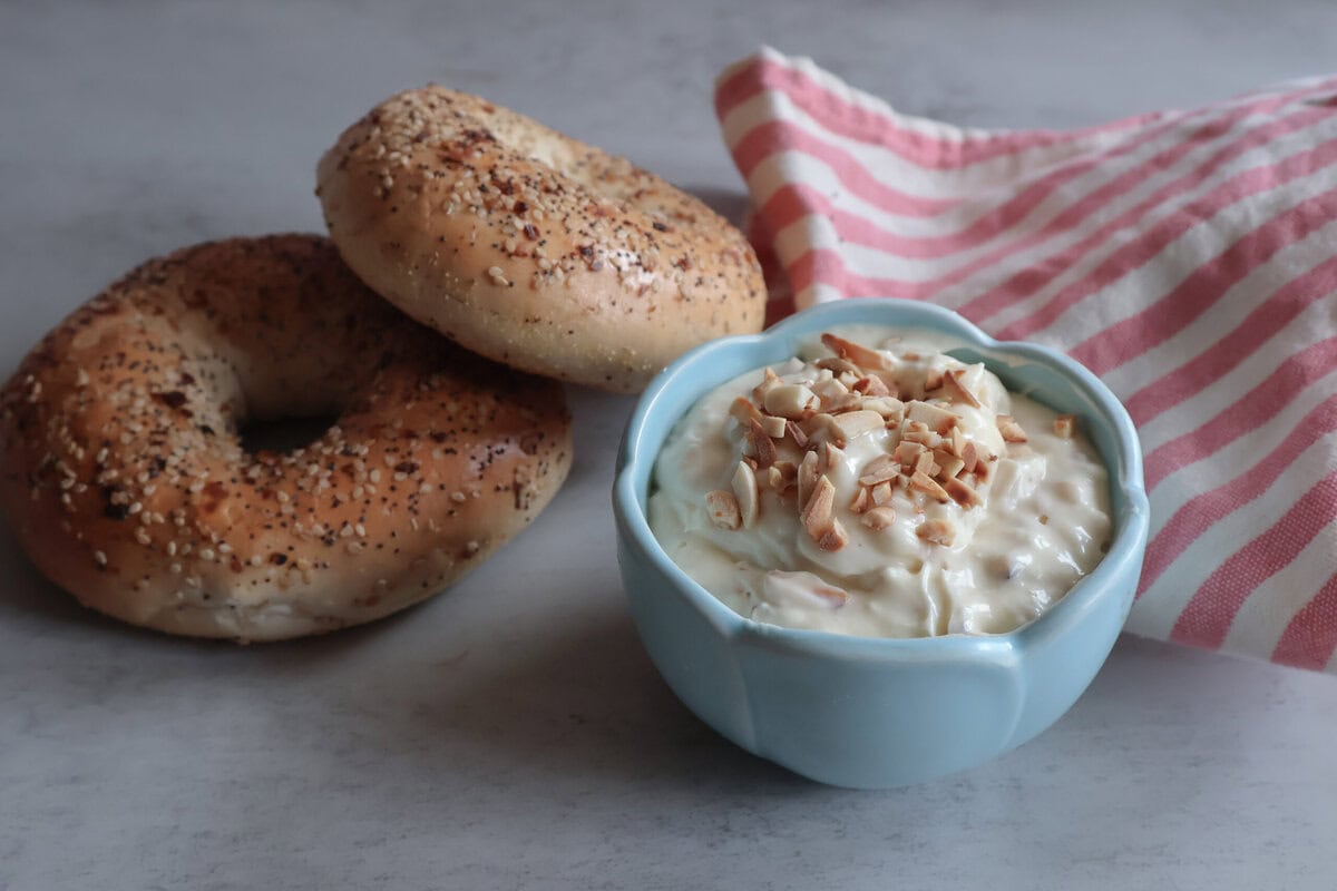 Honey almond cream cheese in a blue bowl with bagels and a pink and white striped tea towel.
