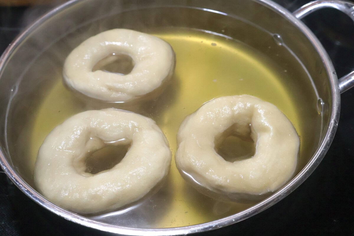 Bagels being boiled in poaching liquid.