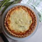 Asparagus and ham quiche on a white plate with a tea towel.