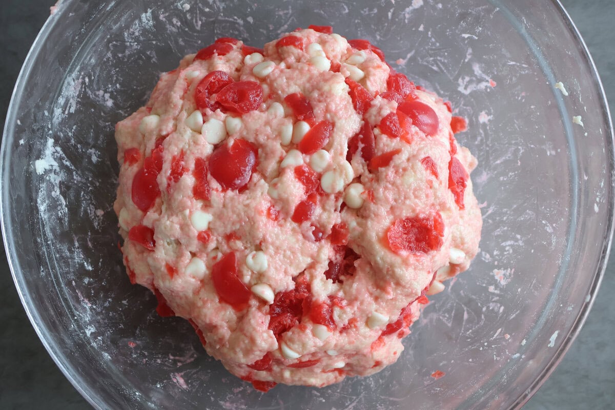 Dough in a glass bowl with cherries and white chocolate mixed in.
