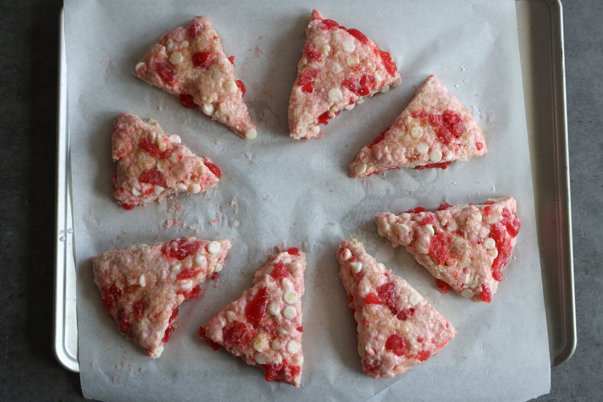 cherry white chocolate scones cut into wedges on a baking sheet.