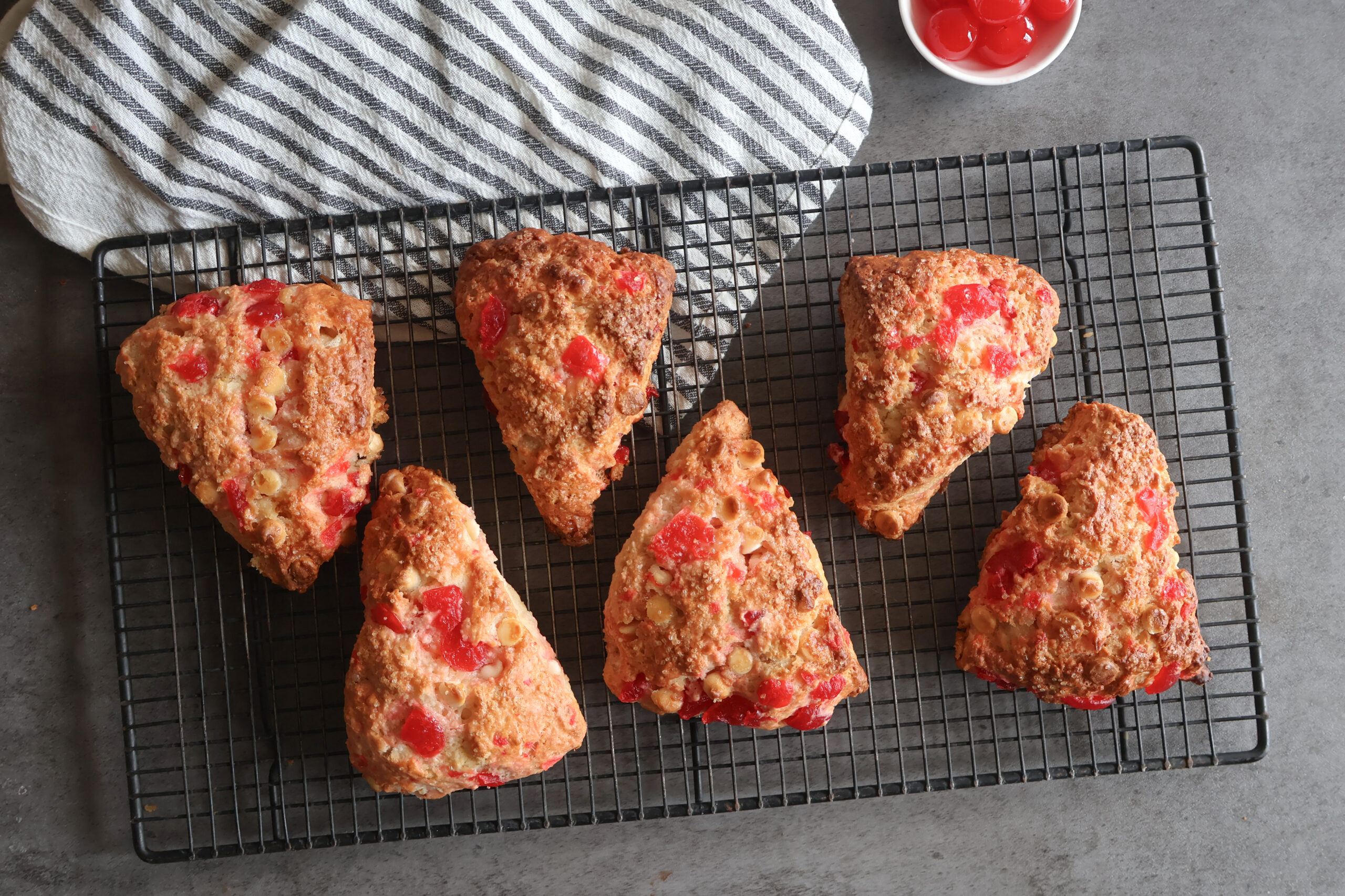 cherry white chocolate scones on a wire rack with a gray striped tea towel.