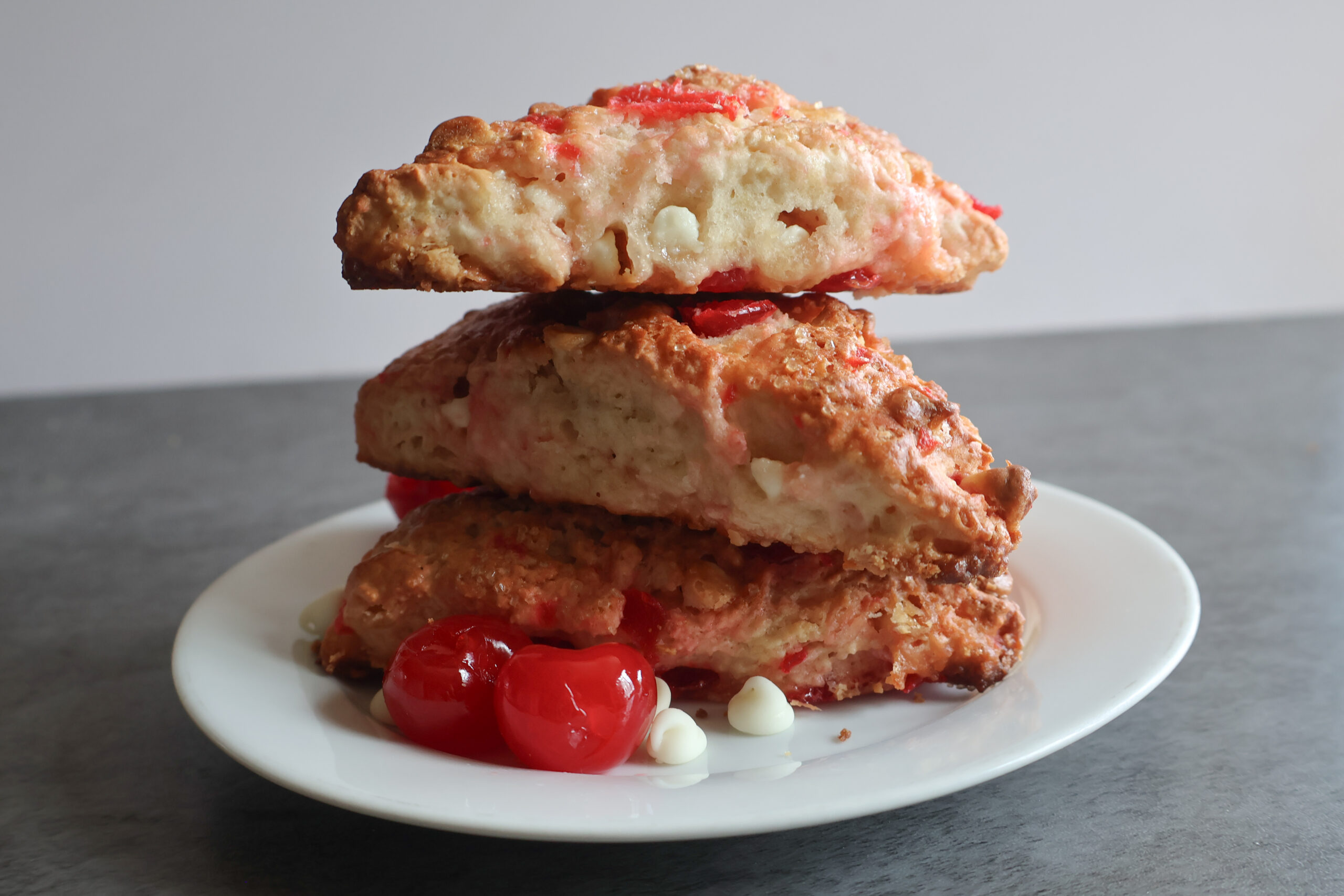 Cherry white chocolate scones piled on top of each other on a white plate.