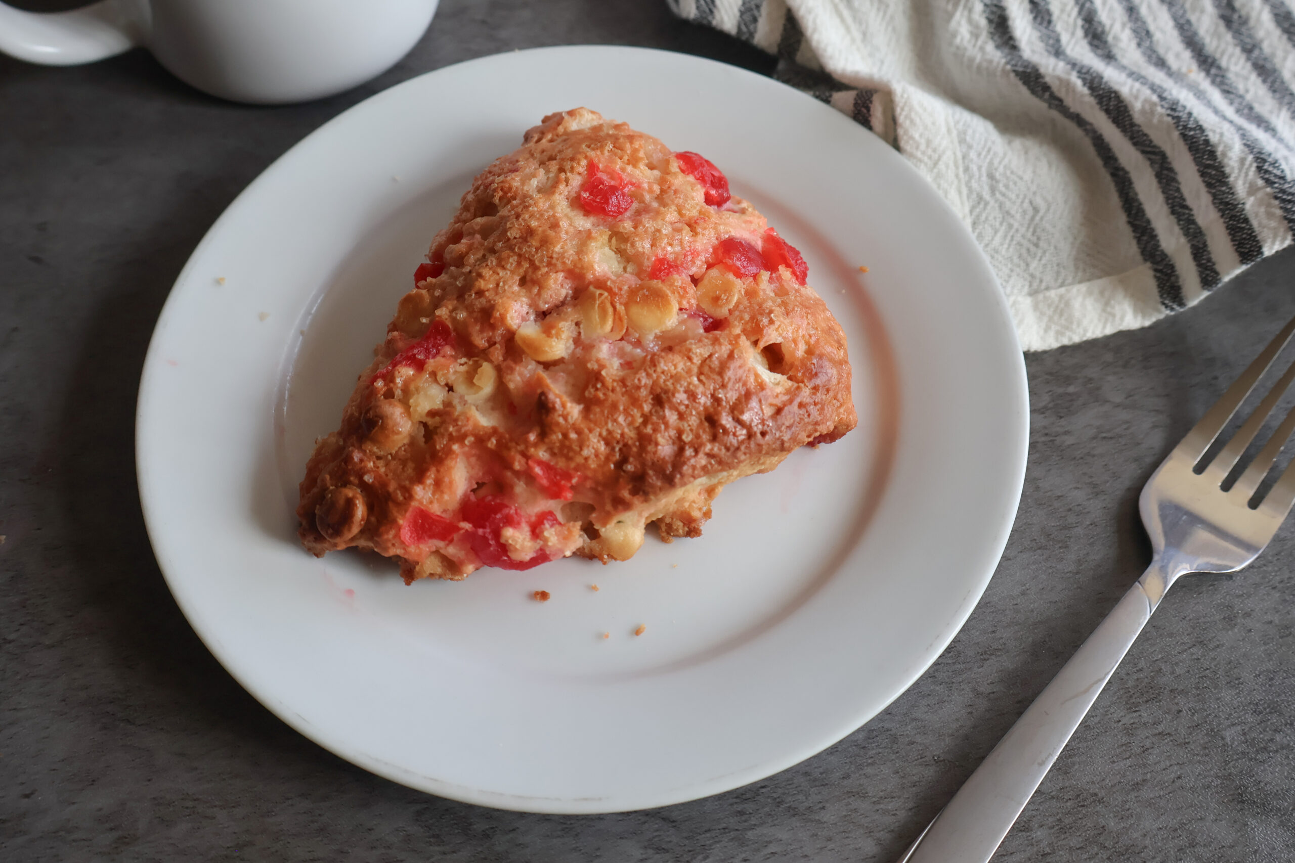 Maraschino cherry white chocolate scone on a white plate with a fork.