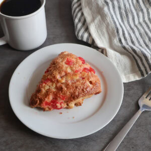 maraschino white chocolate scone on a white plate with a fork and a gray striped tea towel.