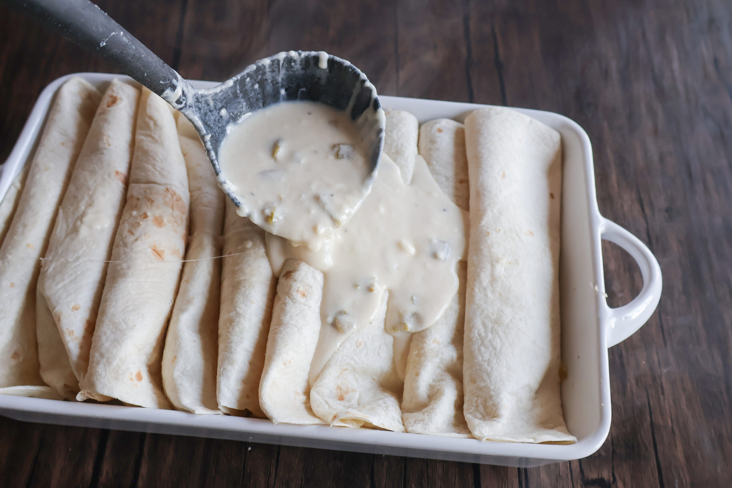 sour cream sauce being spooned on the enchiladas.