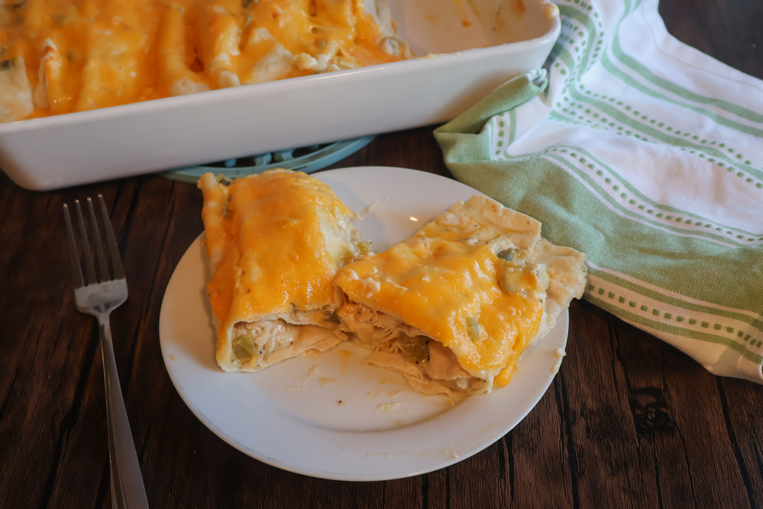 Creamy chicken enchiladas on a white plate with a fork and green and white tea towel.