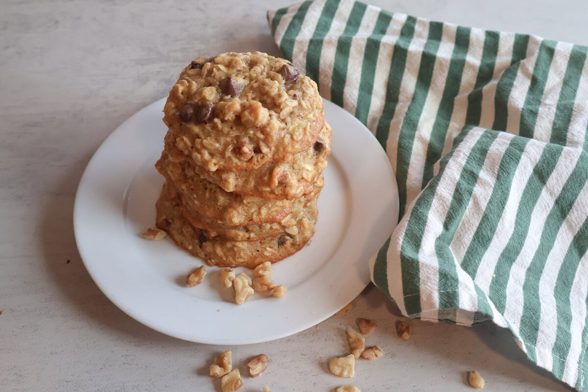Stacked zucchini breakfast cookies on a white plate with a green and white striped tea towel.